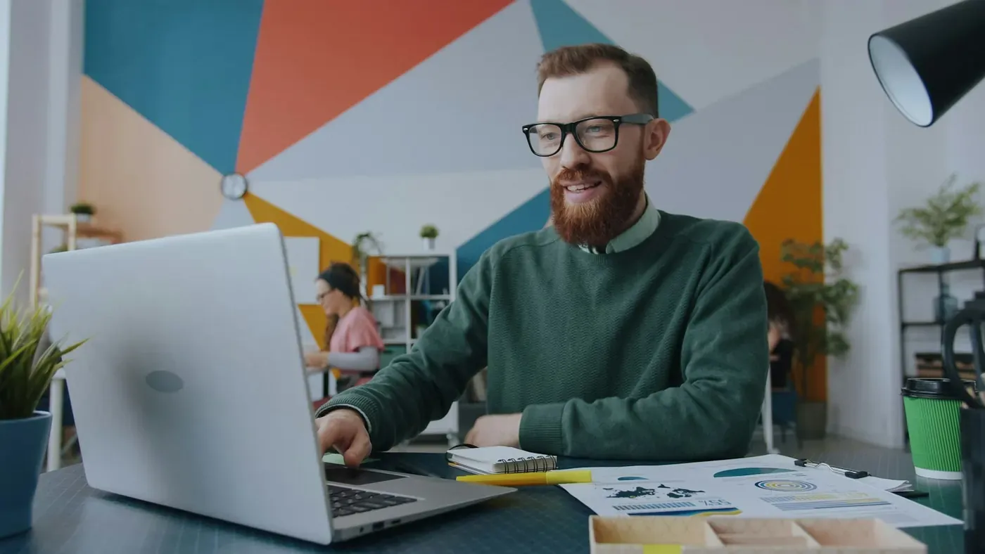 AI consultant smiling at his laptop in a colourful studio, building ad compliance checks into a client's AI workflow with Voxly Vision