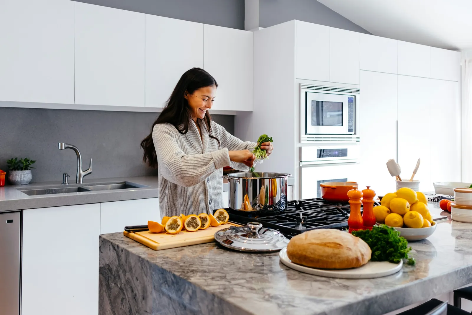 A woman smiling as she cooks with fresh greens, lemons and fruit in a bright kitchen, illustrating everyday healthy living