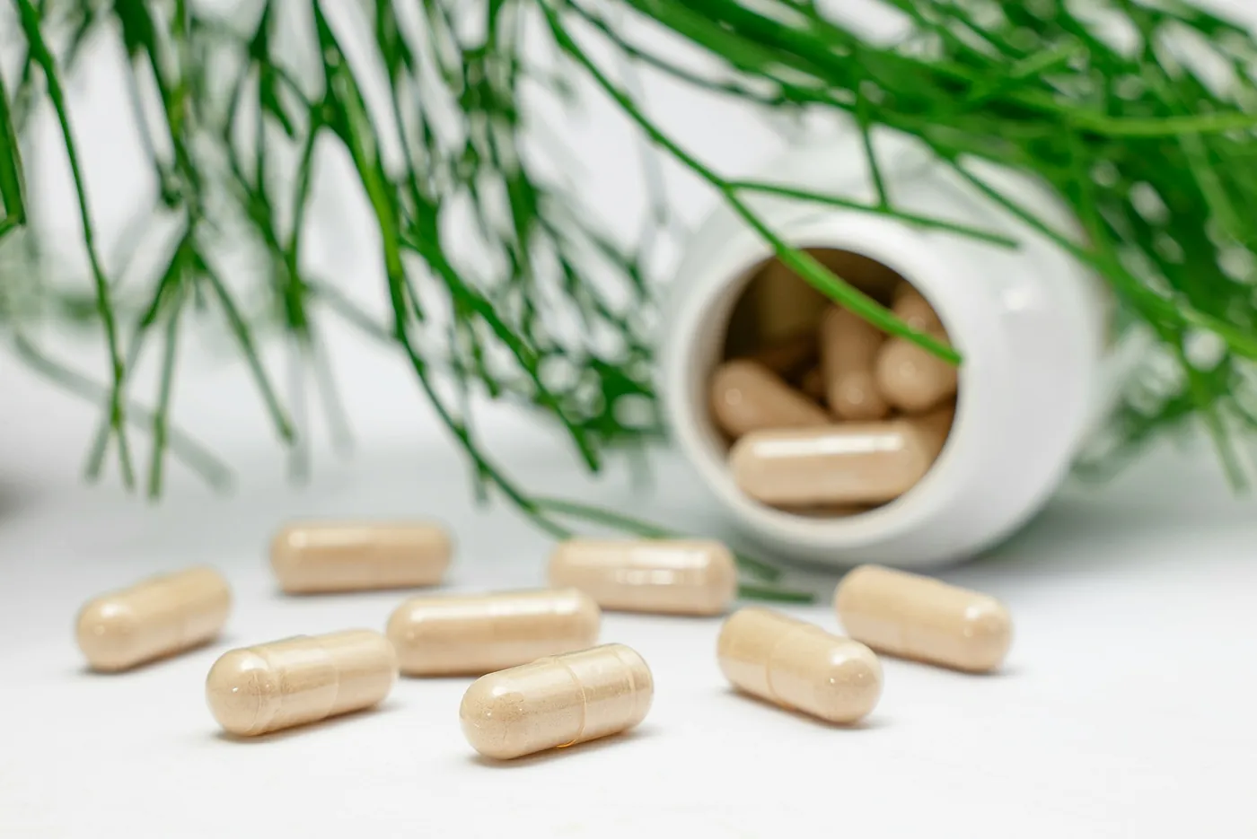 Capsules spilling from a white supplement bottle beside green leaves, typical supplement ad imagery Voxly Vision checks for health claims compliance